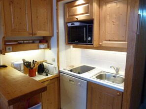 A compact kitchen with wooden cabinets, a microwave, a dishwasher, and a sink.