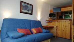 A blue sofa with two colorful pillows, a wooden cabinet with a microwave, and a framed picture on the wall. - 50m from resort center, 12nd floor, view firs, balcony, tv, 29m², Les Arcs (Les Arcs)