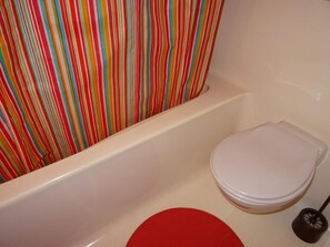 Ein Badezimmer mit einer weißen Badewanne, einem roten Toilettendeckel und einem gestreiften Duschvorhang.