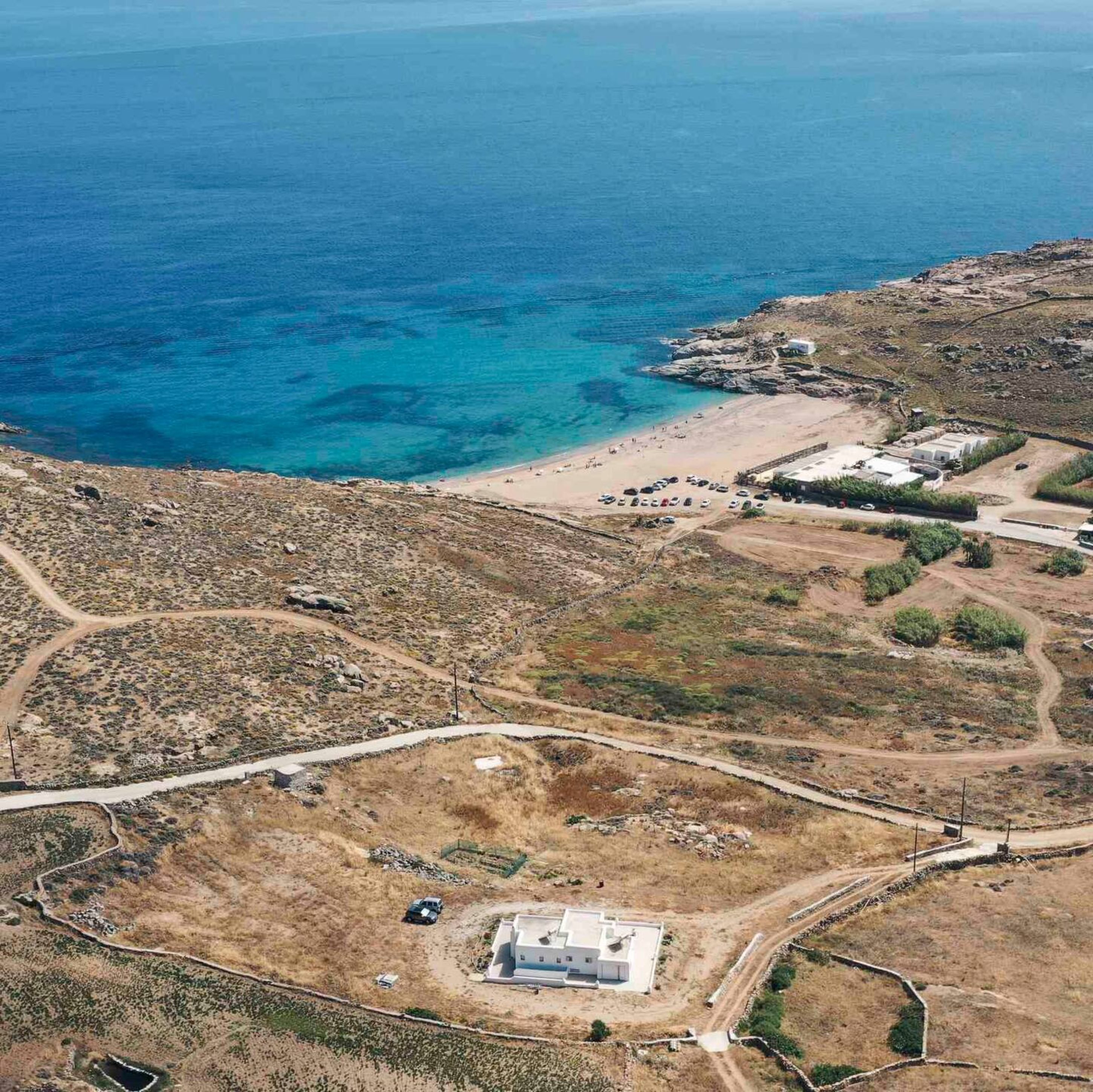 An aerial view of a coastal property with a beach, a parking area, and a building with a flat roof.