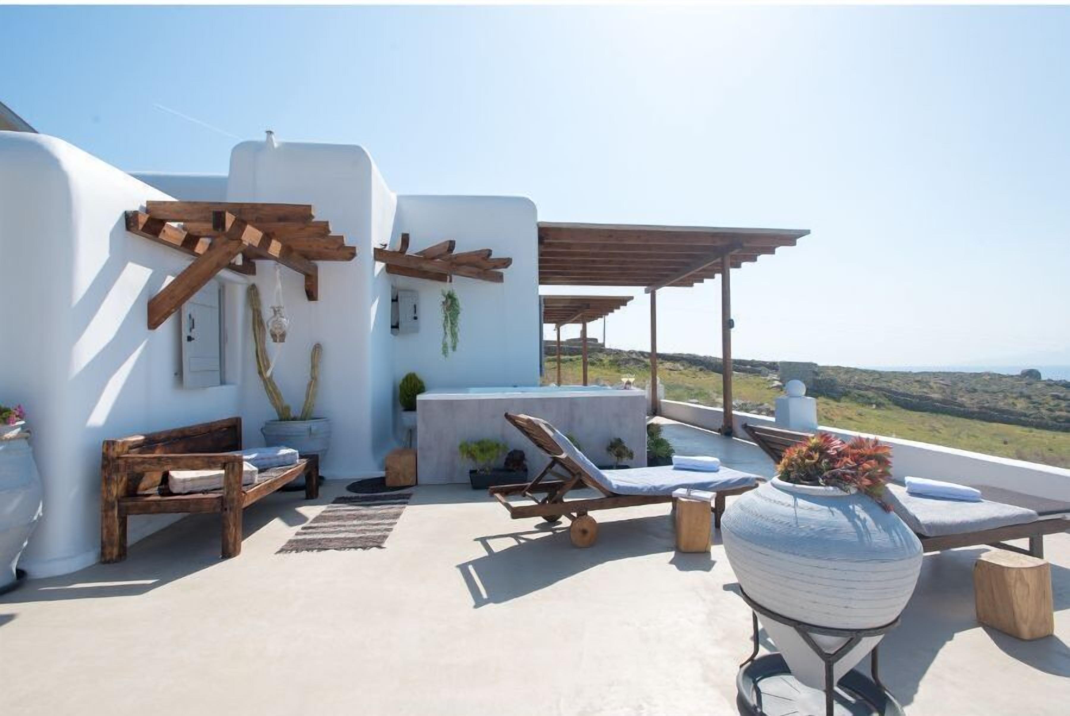 A rooftop terrace with a wooden bench, lounge chairs, and a large vase with flowers.