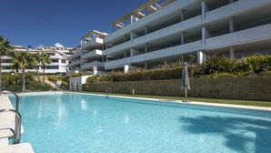 Ett modernt hotell med en swimmingpool, flera balkonger och en vacker, välskött trädgård.