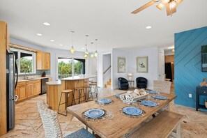 A modern kitchen with wooden cabinets, a dining area with a large wooden table set for six, and a blue accent wall. - AMI Retreat! Pool, Spa, Ping Pong and Walk to Holmes Beach (Holmes Beach)