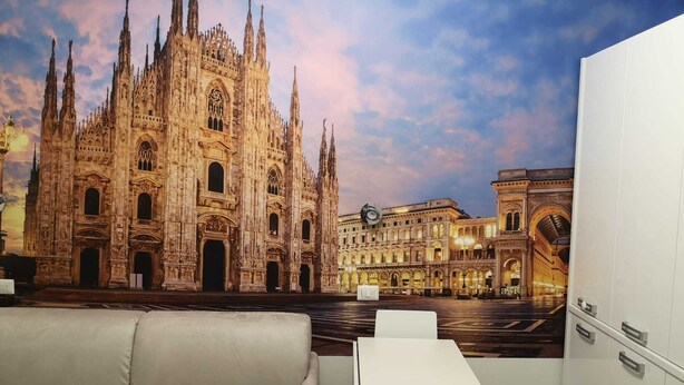 Ein Zimmer mit einer großen Wandmalerei einer Kathedrale und angrenzender Gebäude, einem weißen Sofa und einem kleinen Tisch.