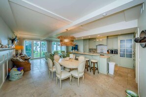 A spacious kitchen with a dining area, large windows, and a hanging light fixture.