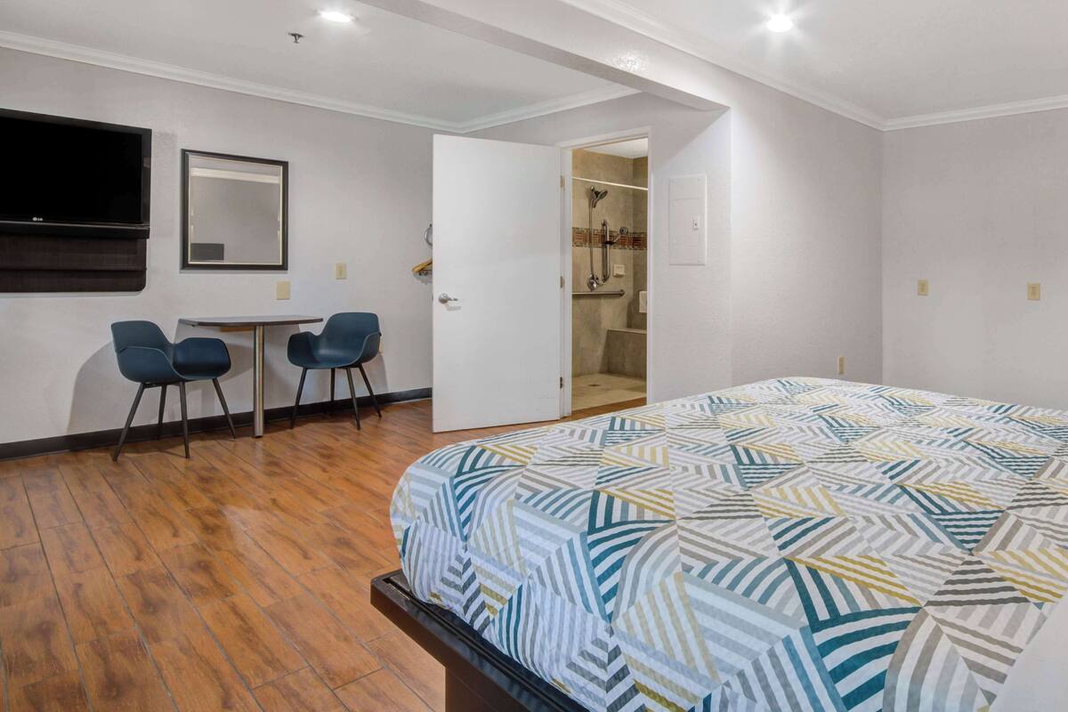 A hotel room with a bed, a desk with two chairs, a TV, and a shower area.