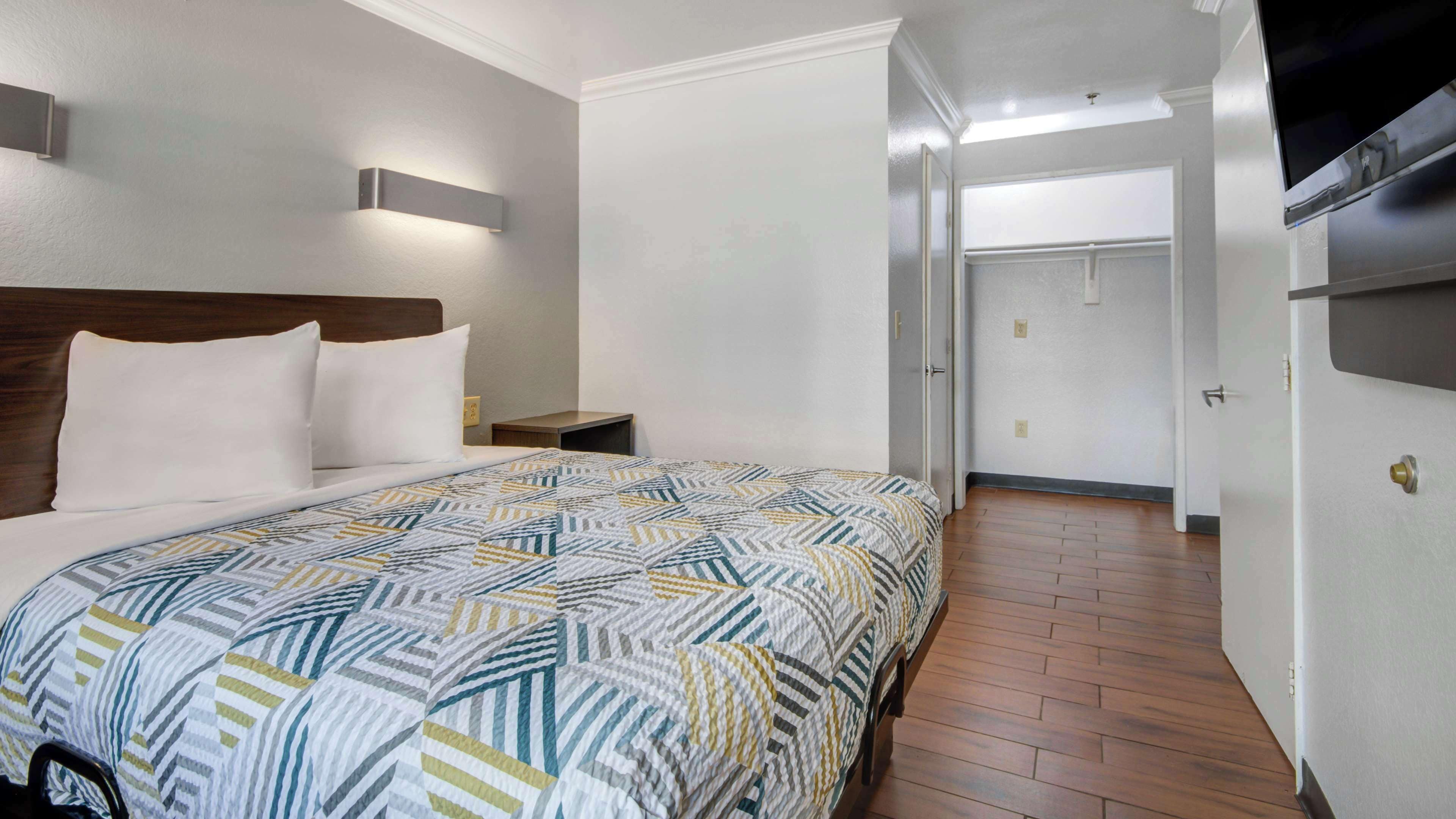 A hotel room with a large bed, a nightstand, a wall-mounted light, and a door leading to another room.