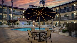 An outdoor pool area with a table and chairs, umbrellas, and a pool. - Studio 6 Ontario, Ca - Convention Center - Airport (Ontario)