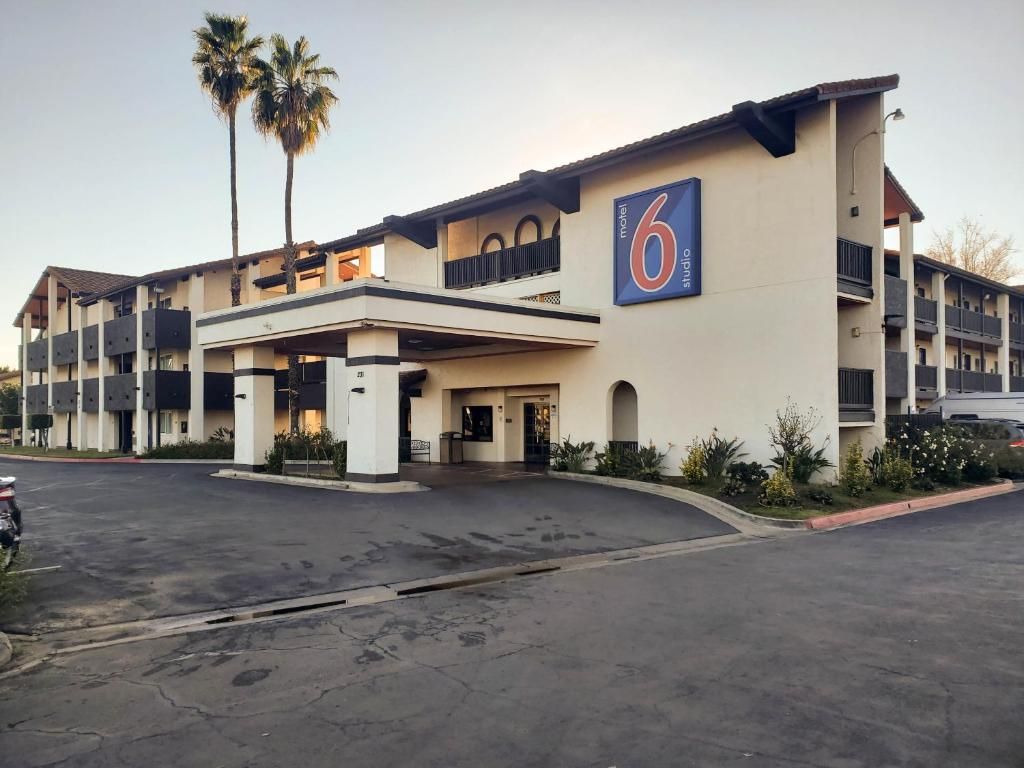 A motel with a large sign reading '6 Motel Studio.' It features a multi-story building with balconies and a parking lot in front.