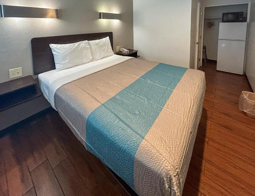 A hotel room with a bed, a nightstand, a wall-mounted light, a microwave, and a refrigerator.