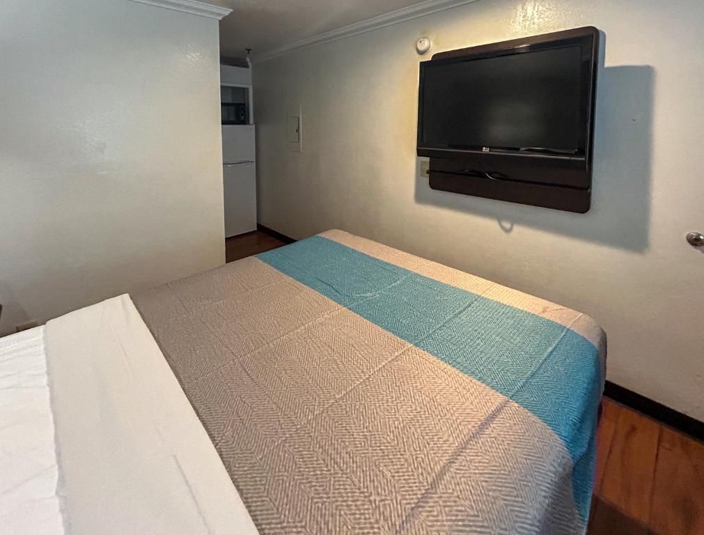 Une chambre avec un lit, un téléviseur fixé au mur et, au fond, une petite cuisine.