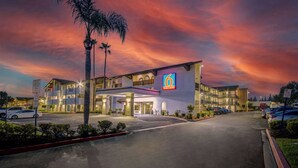 A motel with a '6 Motel + Studio' sign, multiple parking spaces, and a well-lit entrance. - Studio 6 Ontario, Ca - Convention Center - Airport (Ontario)