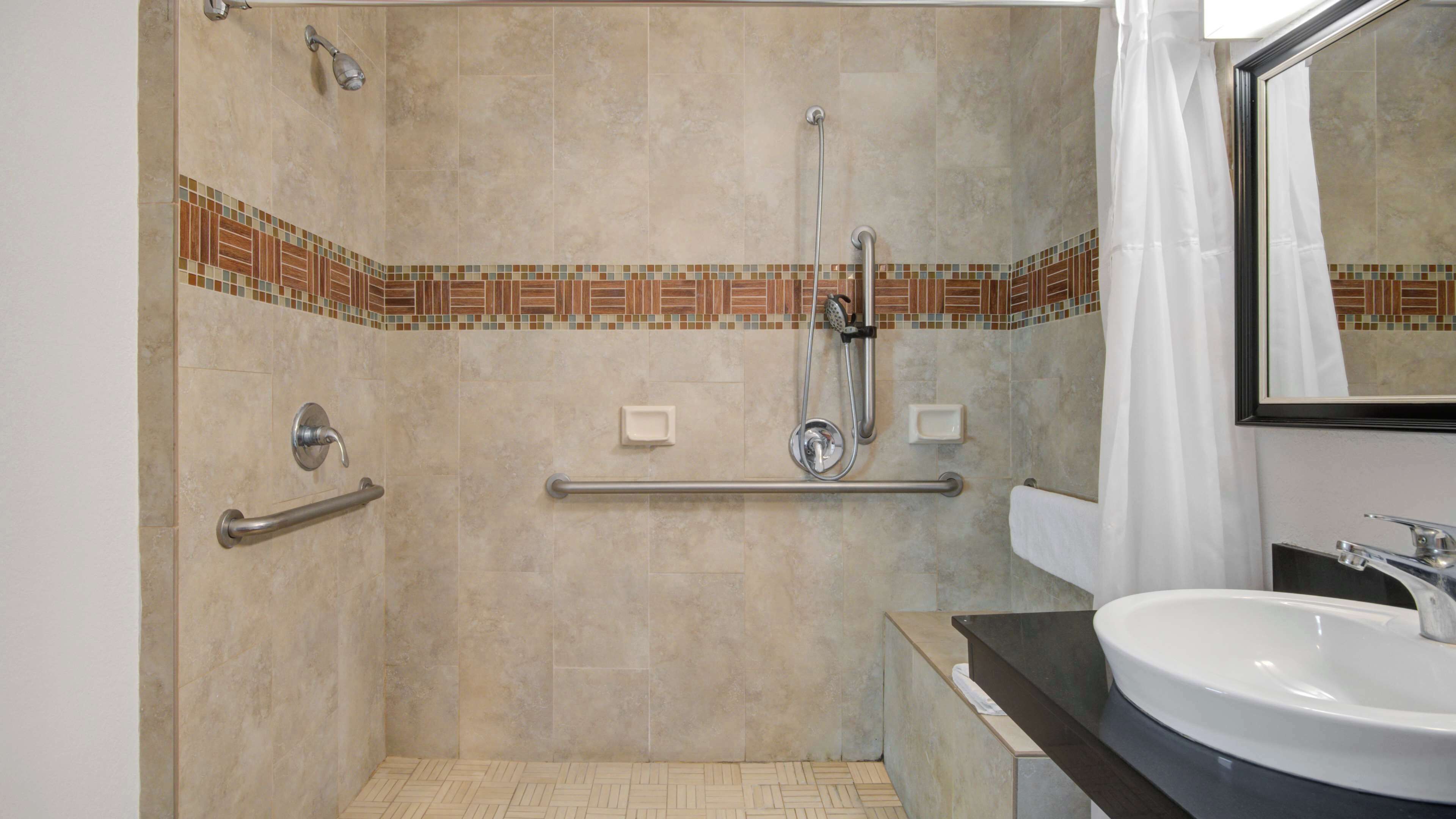 A bathroom with a shower, grab bars, a sink, and a mirror.