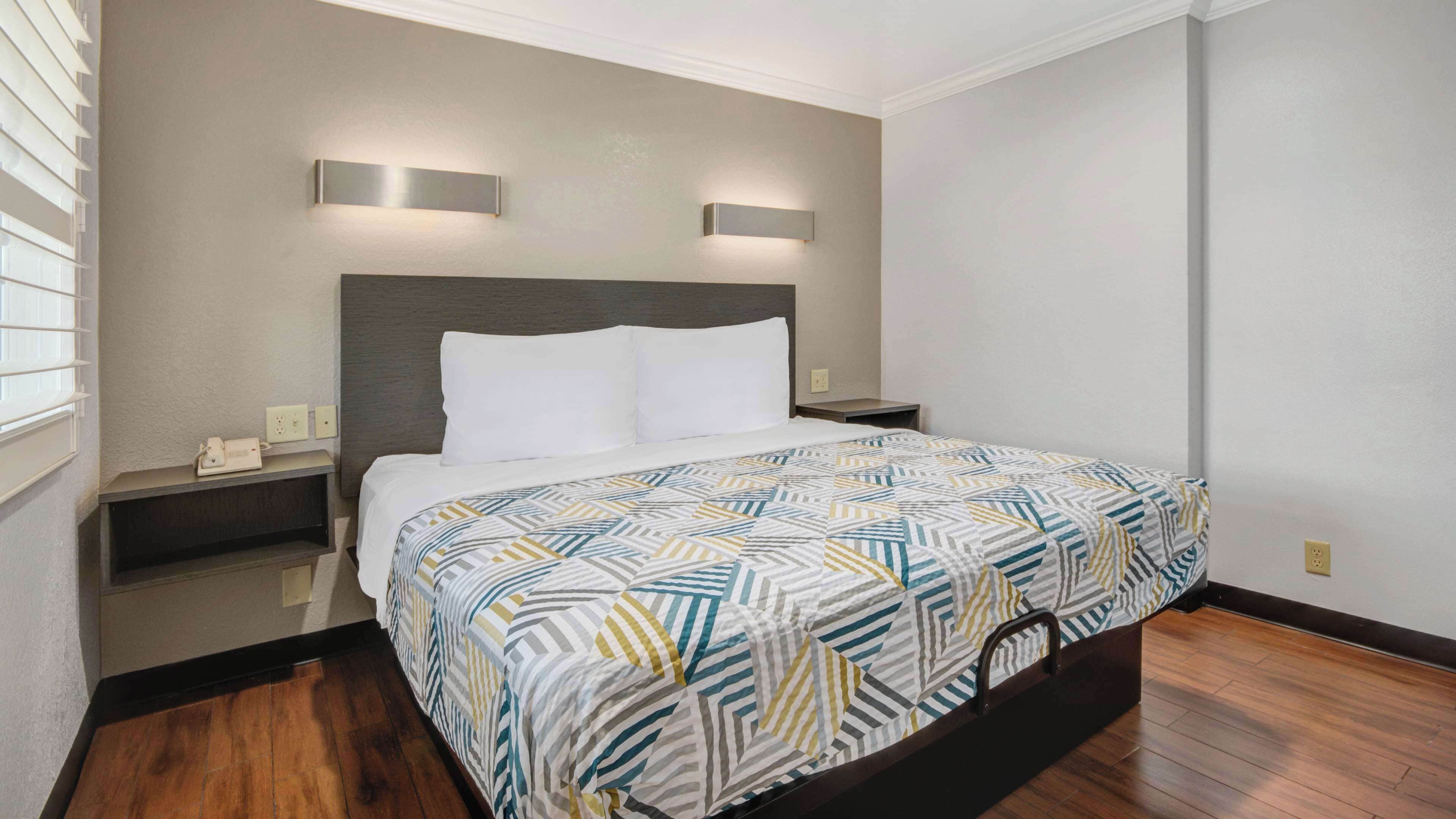 A hotel room with a bed, a nightstand, a wall-mounted light, and a power outlet.