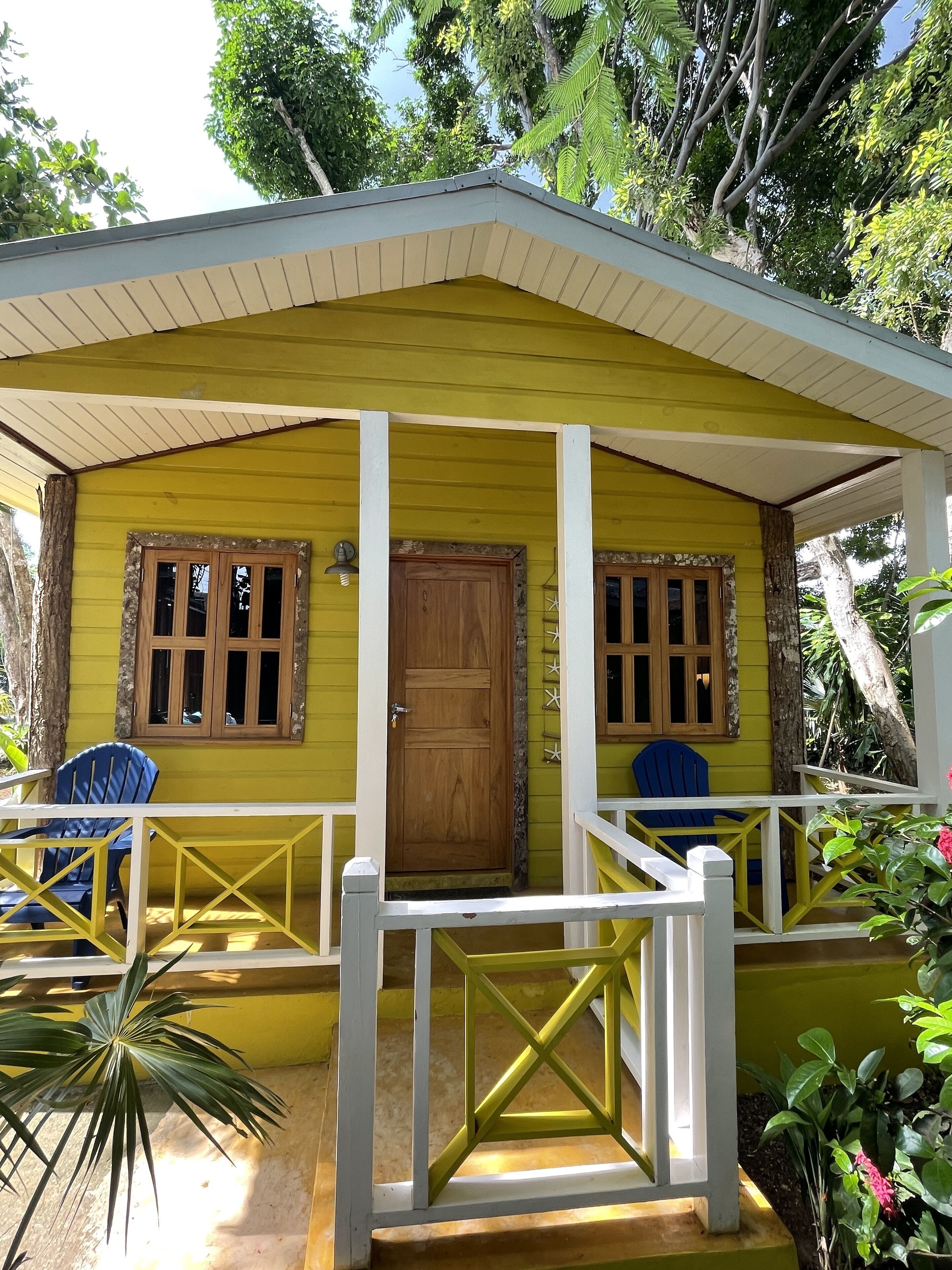 A yellow building with a porch, wooden door, and two windows with shutters.