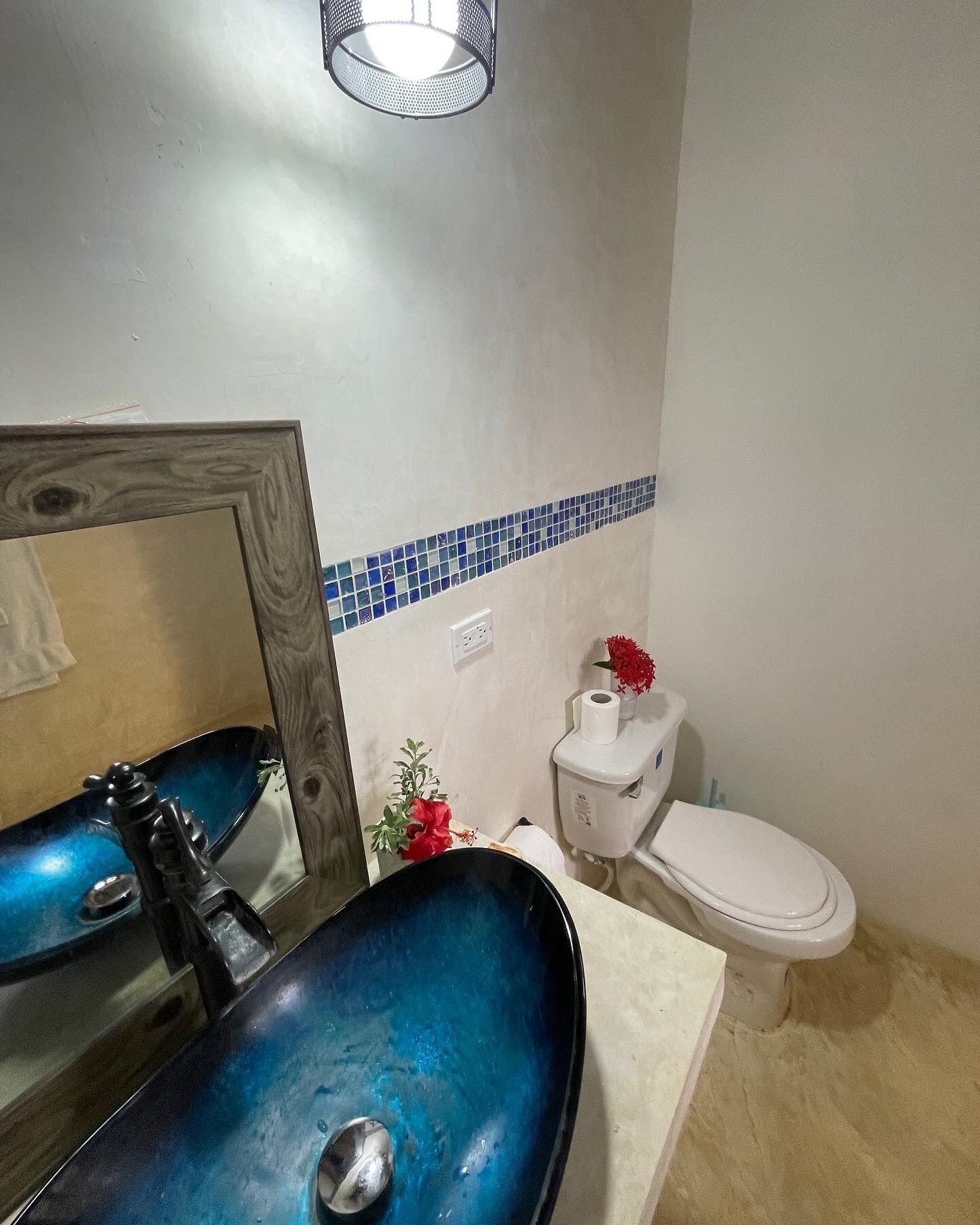 A bathroom with a blue sink, a mirror, a toilet, and a blue-tiled backsplash.