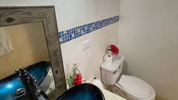 A bathroom with a blue sink, a mirror, a toilet, and a blue-tiled backsplash.
