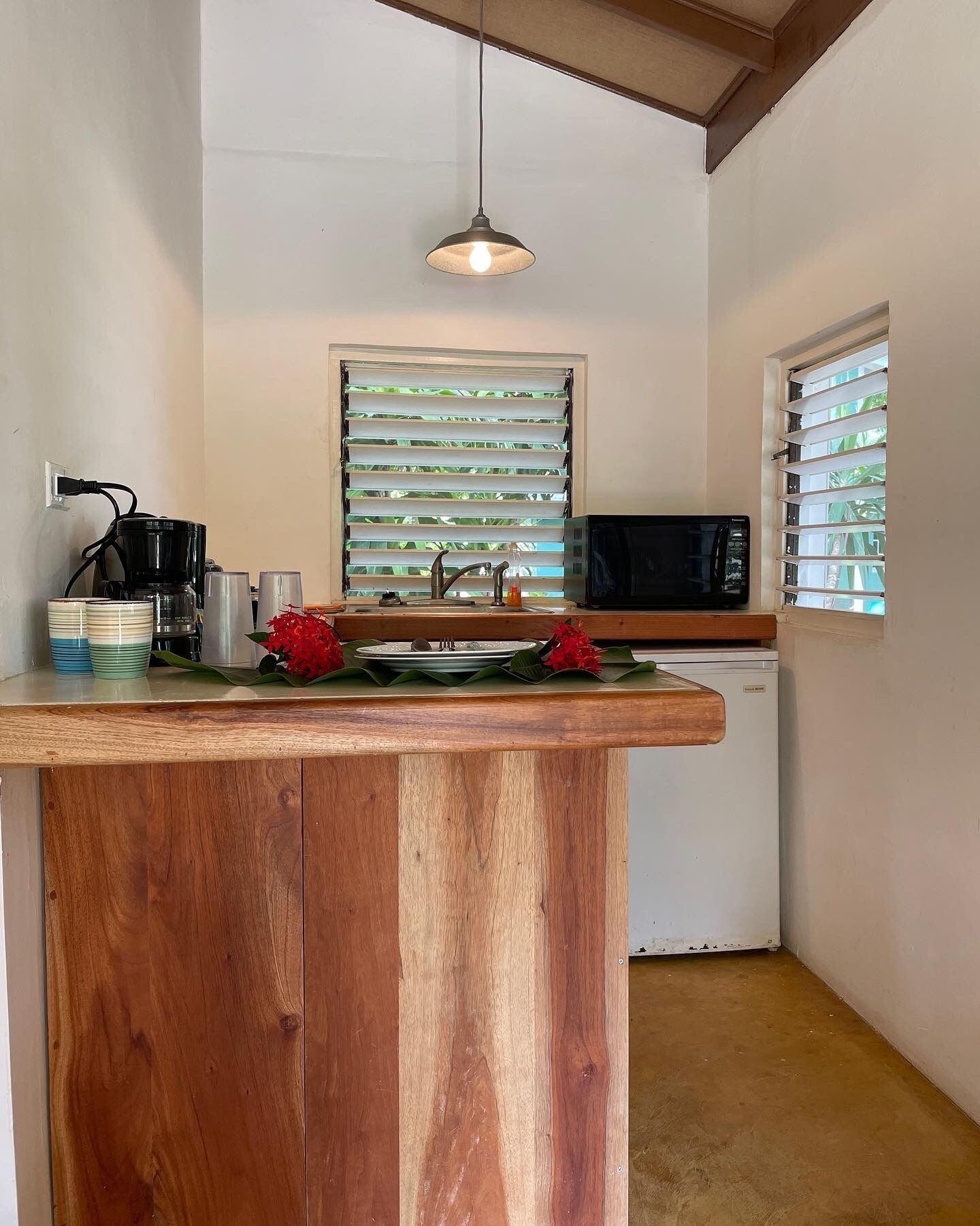 A compact kitchen with a wooden island, a coffee maker, a microwave, and a window with blinds.
