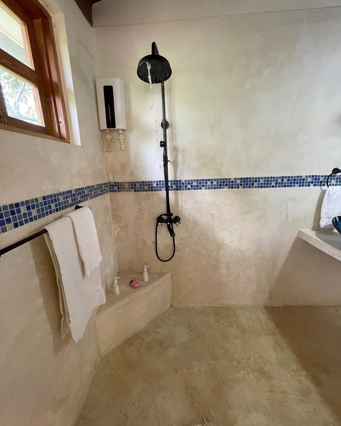 A bathroom with a shower, a towel rack, and a window.