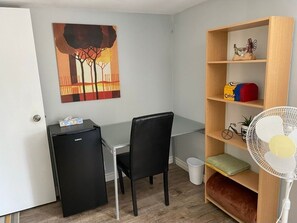 Cozy retreat with a compact layout, featuring a small refrigerator, bookshelf, and comfortable chair.