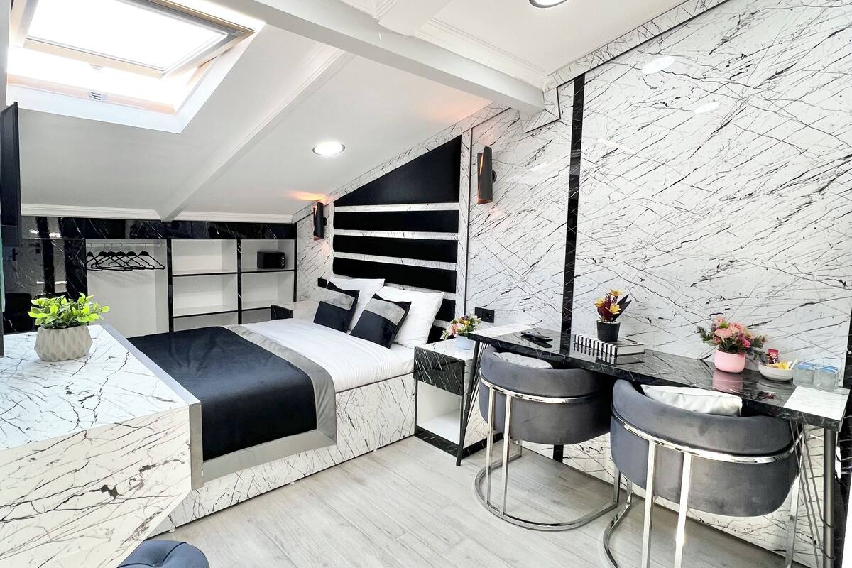 A modern bedroom with a bed, bedside tables, a desk, and a seating area.