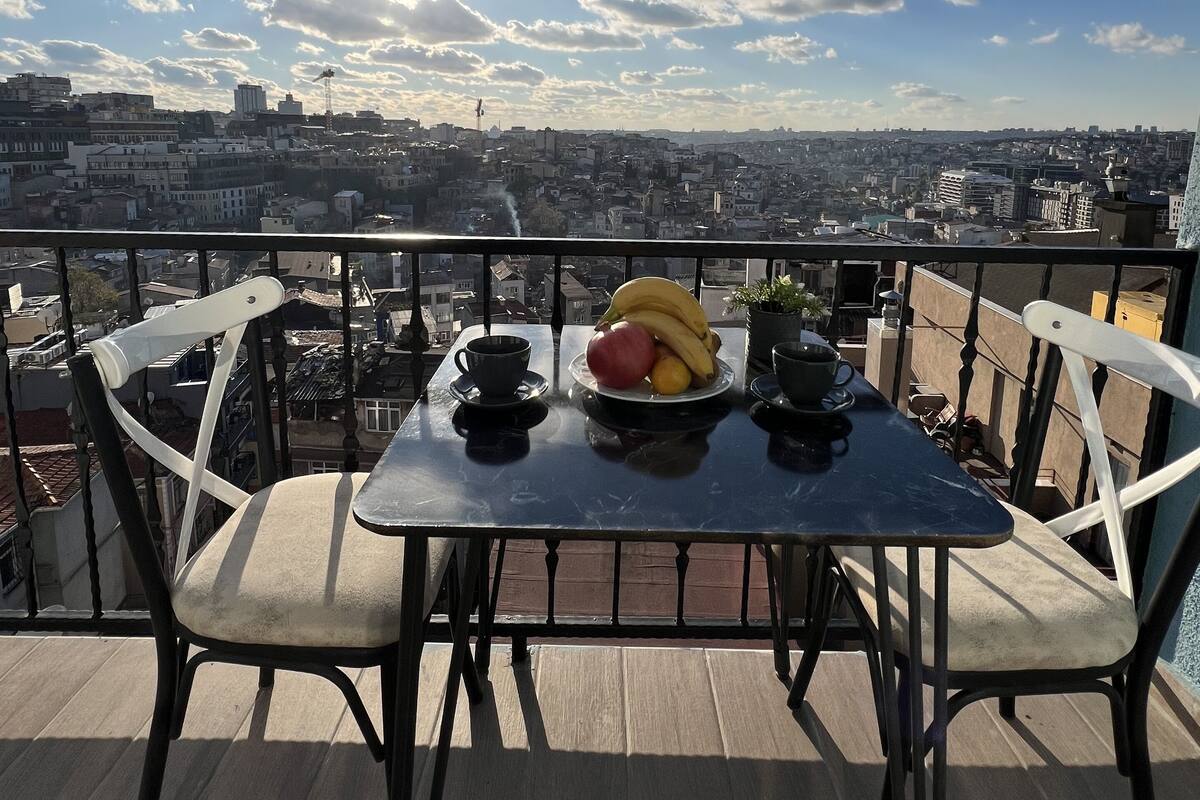 A balcony with a table set for two, featuring a fruit bowl and cups.