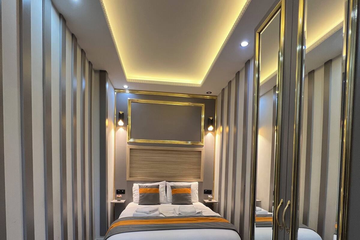A modern hotel room with a large bed, a wardrobe with a mirror, and a ceiling with recessed lighting.
