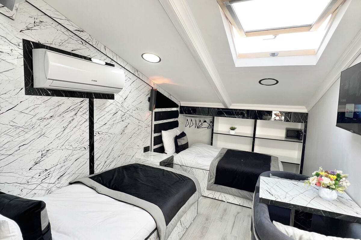 A modern, compact bedroom with a skylight, a bed, a desk, and a seating area.