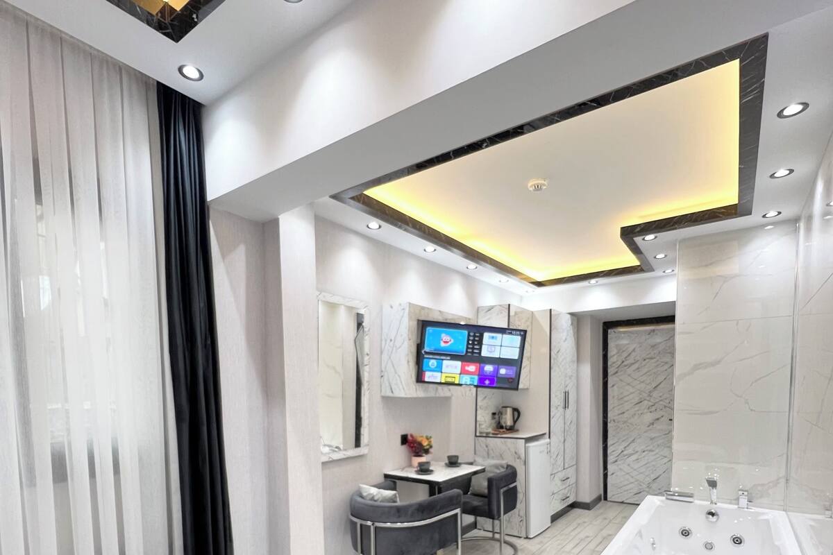 A modern hotel room with a large bed, a bathroom with a bathtub, a vanity with a mirror, and a television mounted on the wall.