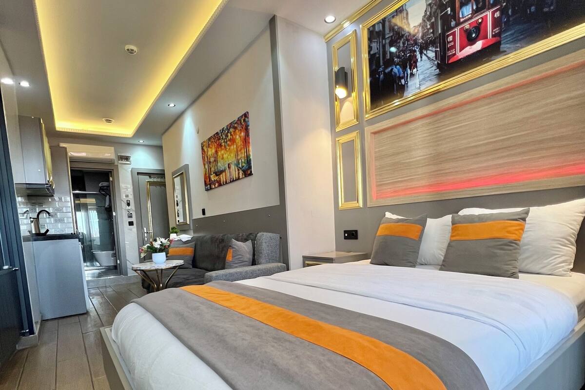 A modern hotel room with a large bed, a dining area, and a kitchen.