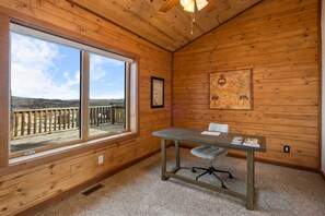 Una stanza con pareti in legno, un'ampia finestra, un tavolo con una sedia e una ventola a soffitto.