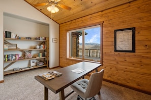 Una stanza con arredamento in legno, un'ampia finestra con vista sulle montagne, una libreria e un tavolo con riviste.
