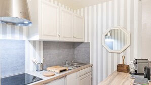 Una cocina con armarios blancos, una campana extractora de acero inoxidable, un fregadero y una cafetera.