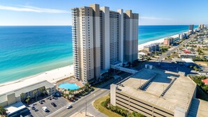 A high-rise hotel with a pool, beachfront view, and a parking lot.