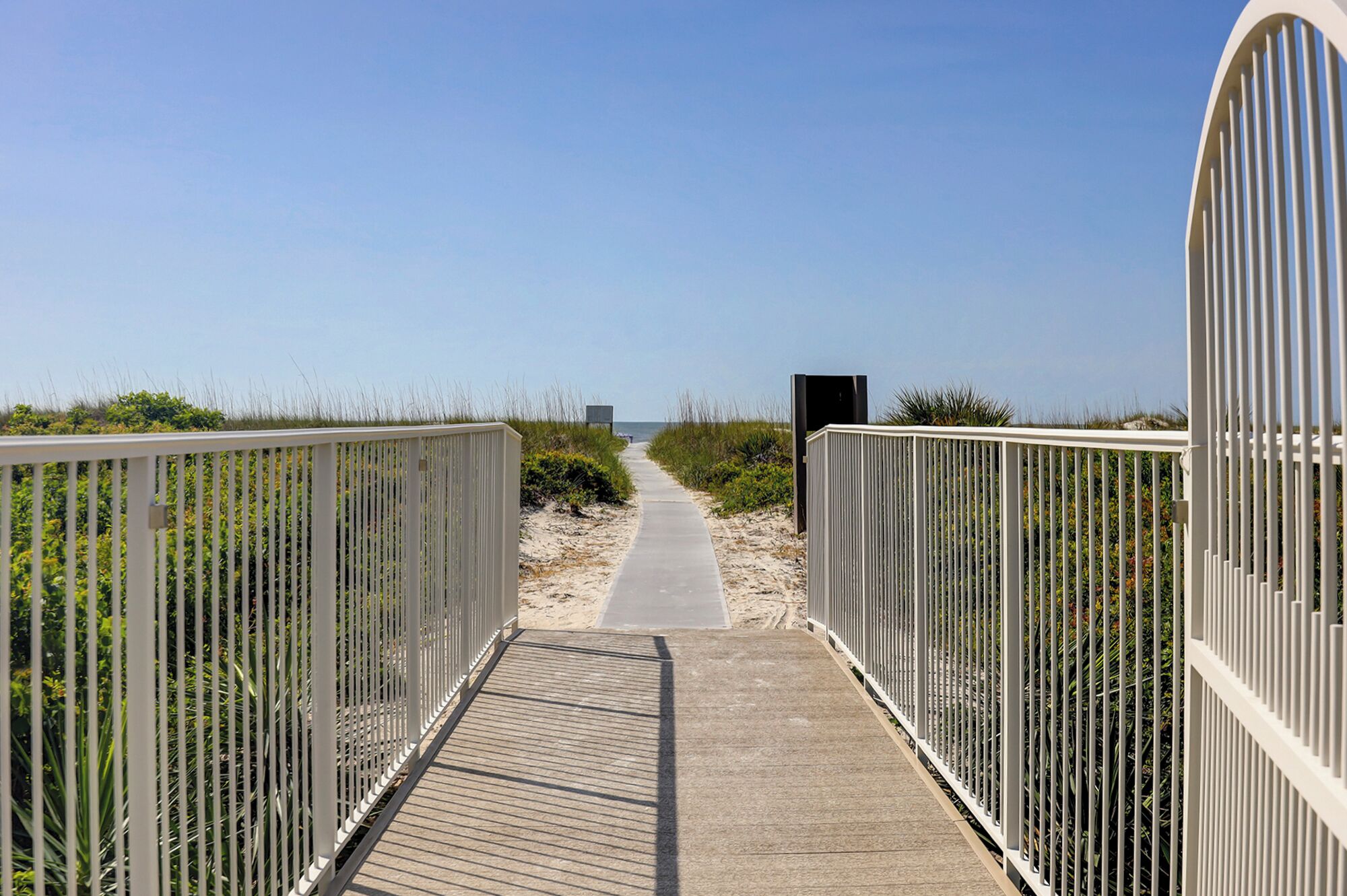 A wooden boardwalk leading to a beach with metal railings on both sides.