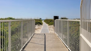Una pasarela de madera que conduce a una playa, con barandas metálicas a ambos lados.