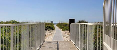 A wooden boardwalk leading to a beach with metal railings on both sides.
