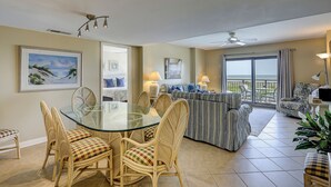 Amplia sala de estar con mesa de comedor de vidrio rodeada por sillas de mimbre, un sofá a rayas y un balcón con vistas.