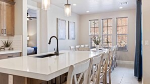 Una cocina moderna con una isla central, iluminación colgante y un comedor con sillas.