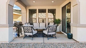 Un patio exterior con una parrilla, zona de estar y ventanas amplias.