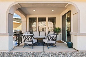 Relax on the patio with a sofa, armchairs, and grill, surrounded by a low wall and lush greenery.