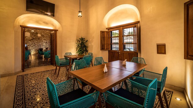Un comedor con una mesa de madera y sillas turquesas, una planta en maceta y vistas a través de un arco.