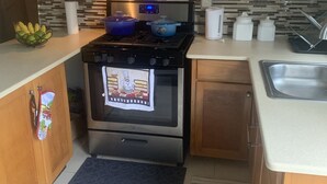 Ett kompakt kök med mikrovågsugn, spis och ugn, träskåp och en kakelbeklädd vägg bakom arbetsbänken.