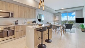 A modern kitchen with a central island, bar stools, a large window, and a flat-screen TV. - One Bedroom Condo King Bed With City Views (Miami)