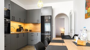 A modern kitchen with grey cabinets, a black refrigerator, and a wooden dining table with black placemats. - Alexander Apartments Airport (Spata-Artemida)