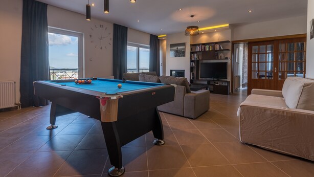 A spacious living room with a pool table, a sofa, a television, and a bookshelf. - Alexander Apartments Airport (Spata-Artemida)