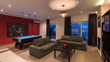 Un salon moderne comprenant une table de billard, deux canapés, une table basse et une bibliothèque.