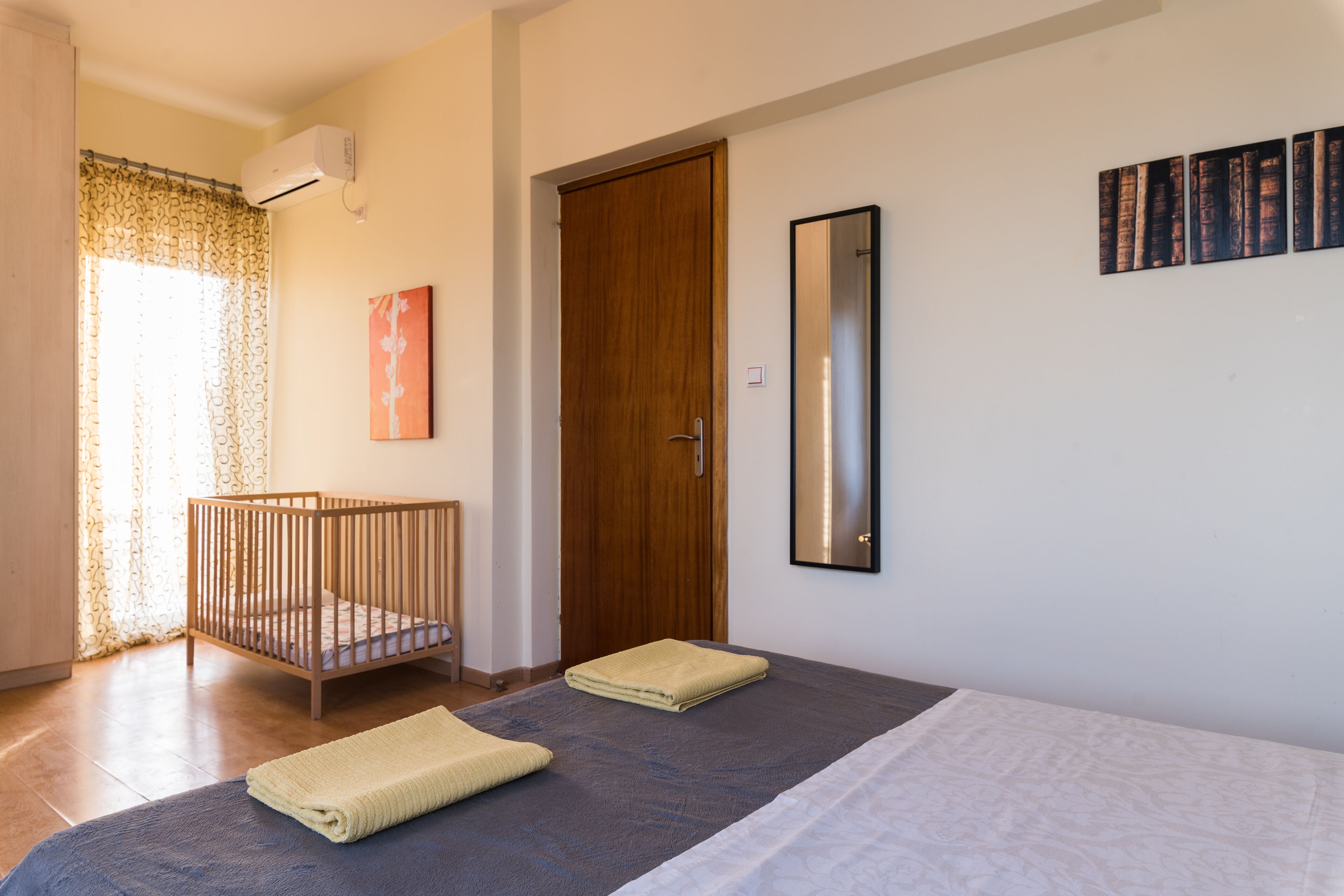 Une chambre avec un berceau, un lit avec des serviettes, une porte en bois et un miroir fixé au mur.