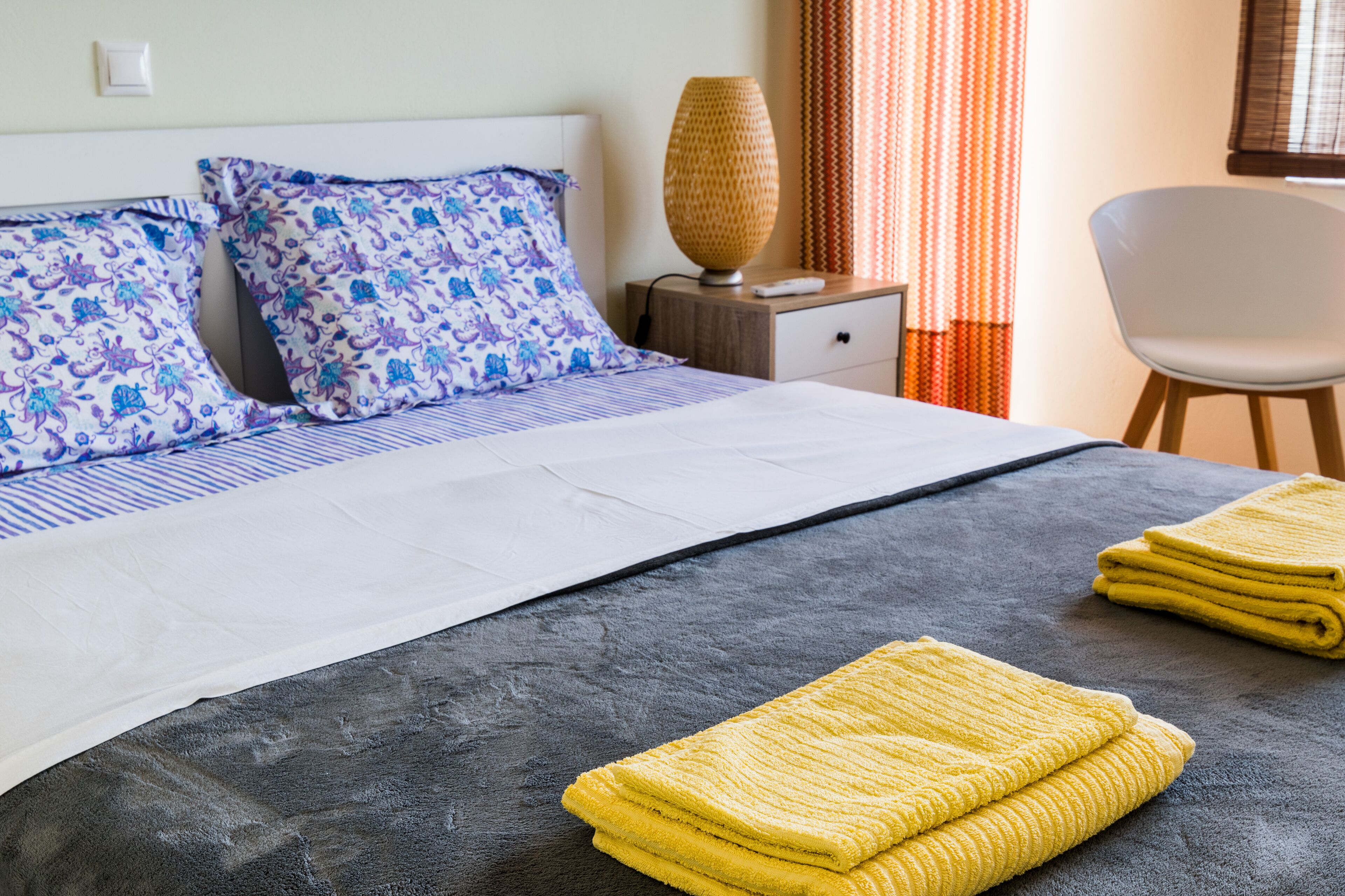A neatly made bed with patterned pillows, a bedside lamp, and a chair.