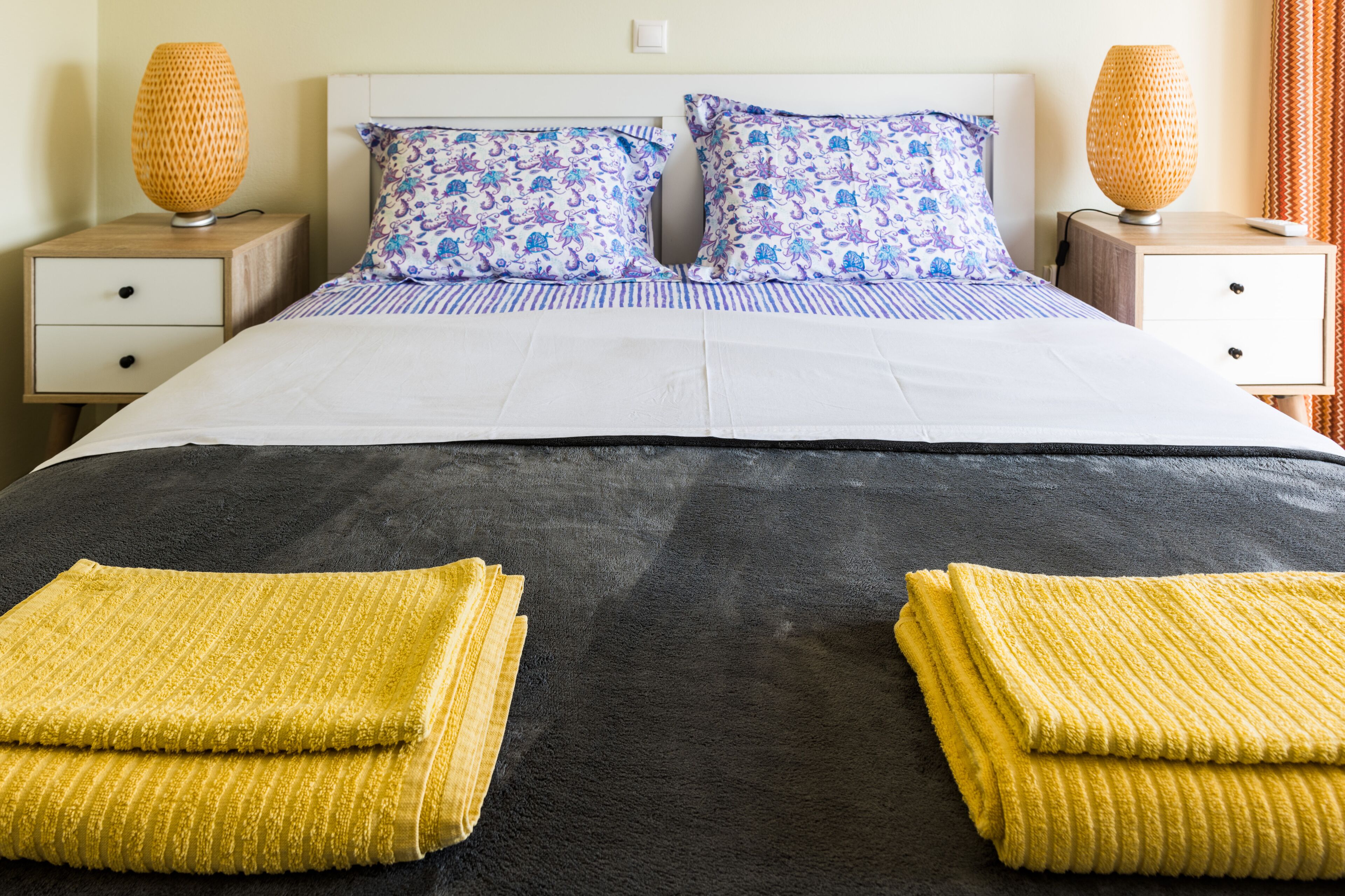 A neatly made bed with a dark headboard, two matching pillows, and a pair of folded towels.